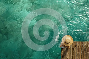 woman wearing sun hat on a wooden pier view from above, turquoise water swimming pool. Summer concept