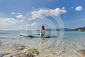 Woman wearing sunglasses sitting on the paddleboard on a water.