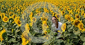 Woman wearing sunglasses standing in field surrounded by sunflowers being photographed by daughter