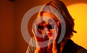 A woman wearing sunglasses is talking on a cell phone in a dark room