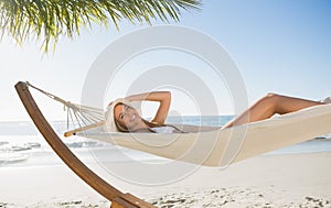 Woman wearing sunhat and bikini relaxing on hammock smiling at camera