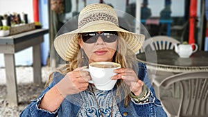 Woman wearing sunhat and sunglasses, drinking coffee from a huge coffeecup