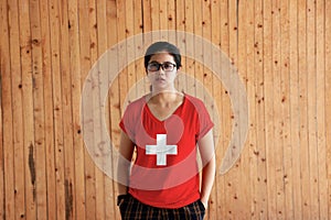 Woman wearing Switzerland flag color shirt and standing with two hands in pant pockets on the wooden wall background