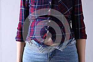 Woman wearing tight jeans and shirt on light grey background, closeup. Overweight problem