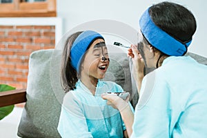 a woman wearing a towel applies a black clay face mask with a brush to the little girl& x27;s face