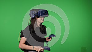 A woman wearing virtual reality glasses and with joysticks on a green background