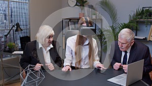 Woman wearing virtual reality glasses tries 3D app for VR helmet while colleagues supporting her