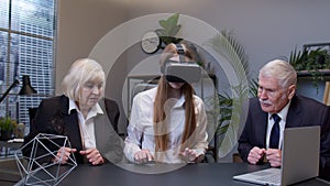 Woman wearing virtual reality glasses tries 3D app for VR helmet while colleagues supporting her