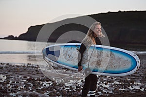 Woman Wearing Wetsuit Carrying Surfboard As She Walks Out Of Sea