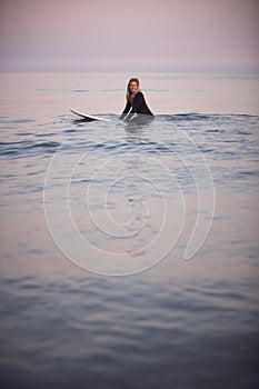 Woman Wearing Wetsuit Sitting And Floating On Surfboard On Calm  Sea