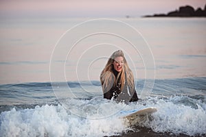 Woman Wearing Wetsuit Sitting On Surfboard Riding Wave Into Beach