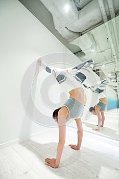 Woman wearing white and grey leggings practicing arm stand