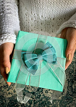 Woman wearing white sweater  giving a blue present.