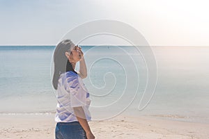 Woman wearing white t-shirt, she standing on sand beach and holding sunglasses in hand with beautiful seascape view.