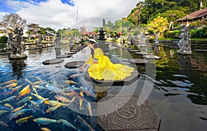 Woman wearing yellow dresses to feed koi fish in Taman Tirtagangga temple on Bali,Indonesia