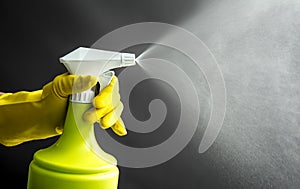 Woman wearing yellow rubber gloves and using gardening spray bottle.