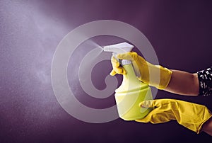 Woman wearing yellow rubber gloves using green spray bottle.