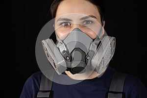 A woman wears a protective respirator with dust and gas filters on a black background.