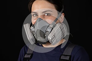 A woman wears a protective respirator with dust and gas filters on a black background.