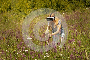 Woman weating virtual reality headset sitting in the middle of a field of flowers. Immersive VR experience