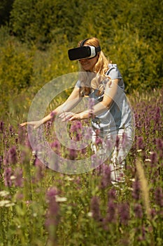 Woman weating virtual reality headset sitting in the middle of a field of flowers. Immersive VR experience