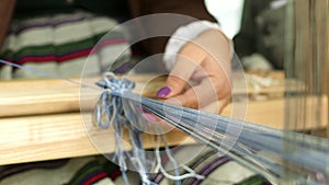 Woman weaves a blue garter on a loom.