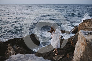 a woman in a wedding dress stands by the ocean on a cliff