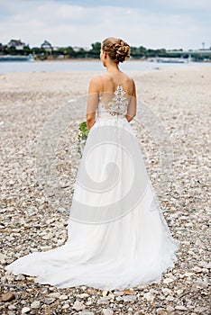 a woman in a wedding gown walks on a beach with rocks