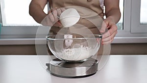 woman weighing flour in a plate on a kitchen scales, dough and pastry preparation