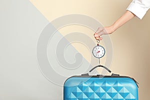 Woman weighing suitcase against color background