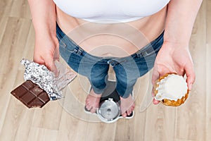 woman weighs on scales, chocolate in her hands