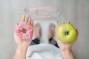 woman on weight scale and hand hold green Apple and donut, choose between fruit is Healthy and sweet is Unhealthy junk food.