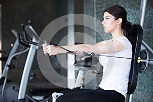 Woman weight training at gym. Exercising on pull down weight machine. Woman doing pull-ups exercising lifting dumbbells.