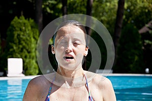 Woman with wet face in summer pool water on vacation