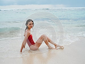 Woman with wet hair after swimming in the ocean in a red swimsuit lies sexily on the beach in Bali, travel to Indonesia