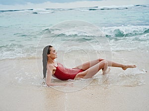 Woman with wet hair after swimming in the ocean in a red swimsuit lies sexily on the beach in Bali, travel to Indonesia
