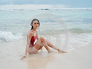 Woman with wet hair after swimming in the ocean in a red swimsuit lies sexily on the beach in Bali, travel to Indonesia