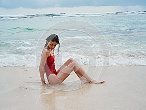 Woman with wet hair after swimming in the ocean in a red swimsuit lies sexily on the beach in Bali, travel to Indonesia