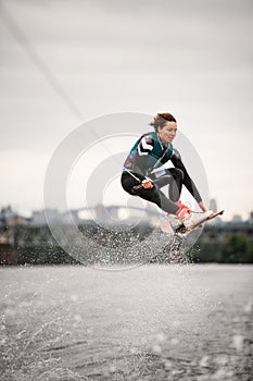 Woman in wetsuit holding rope and professionally jumping over water on wakeboard photo
