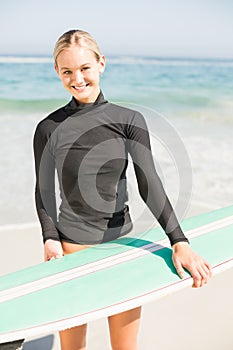 Woman in wetsuit holding a surfboard on the beach