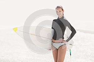 Woman in wetsuit holding a surfboard on the beach