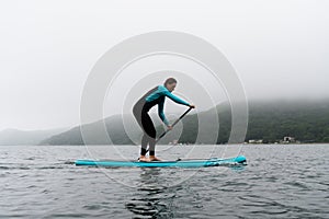 A woman in a wetsuit paddle a paddleboard with an oar on the sea waves in cloudy weather.