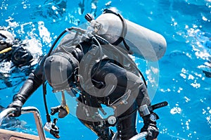 A woman in a wetsuit with a scuba gear rises to the deck of a yacht.