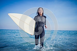 woman in wetsuit with a surfboard on a sunny day