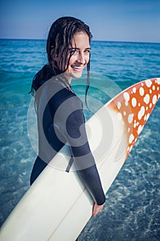 woman in wetsuit with a surfboard on a sunny day