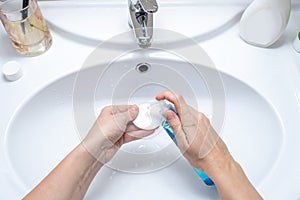 Woman wetting a cotton pad with a micellar make up remover, cleansing and purifying face skin