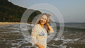 Woman is Wetting her Hair in a White Tunic on the Beach, near the Sea. Blonde in Sunglasses. Tourist Enjoying Vacation