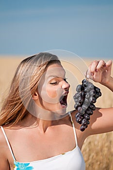 Woman in wheat field eating grapes. Summer picnic.