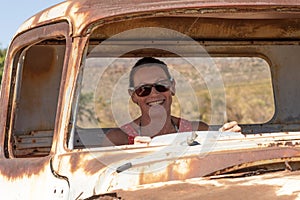 Woman at the wheel of a rusty car.