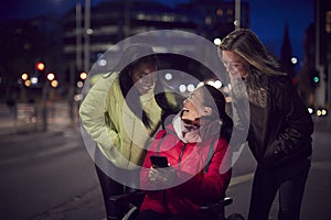 Woman In Wheelchair Having Night Out With Friends In City Ordering Taxi Using Mobile Phone App